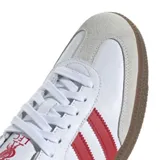 Championes Adidas modelo Samba, de diseño clásico con base de cuero blanco, franjas laterales rojas, puntera de gamuza gris y suela de goma color caramelo.