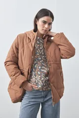 Campera puffer color tostado con diseño acolchado de costuras geométricas, capucha integrada, cierre frontal con cremallera y botones a presión, y bolsillos laterales.