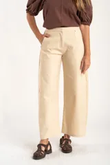 Pantalón de corte baggy y tiro medio, confeccionado en algodón peinado de color arena. Presenta diseño de pierna ancha, cierre frontal con botón y bolsillos laterales.