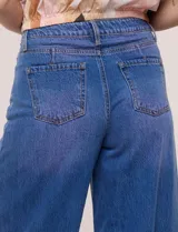 Jean wide leg cropped de tiro medio-alto, confeccionado en denim azul intermedio con efecto degradé y costuras en tono camel. Presenta cinco bolsillos, cierre frontal con botón y cierre, nervaduras decorativas en la zona de las rodillas y ruedo desflecado.