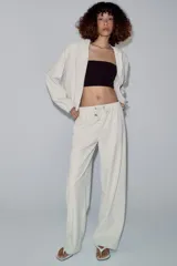 Pantalón de tiro medio color beige, de pierna ancha y corte recto. Cuenta con cintura elástica ajustable con cordones y bolsillos frontales.