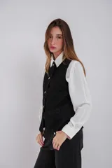 Chaleco entallado de jean negro con cuello a la base, cierre frontal con botones, bolsillos simulados y abertura en la parte trasera.