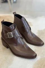 Botin de cuero color bordó, con diseño de puntera cuadrada y detalle de hebilla metálica lateral. Presenta una textura combinada en el lateral y suela de goma negra.