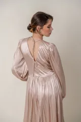 Vestido largo de satén color champagne, con escote en V profundo y mangas largas abullonadas con puños elásticos. Presenta apliques bordados con lentejuelas en el escote y la cintura.