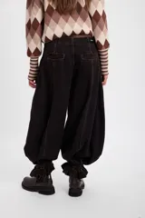 Jean de corte wide leg con efecto degradado en tonos marrón y negro. Presenta costuras verticales frontales y un diseño de puño ajustable en el bajo de la pierna.