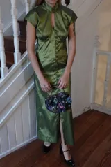 Vestido largo verde de tafeta con silueta entallada, cuello alto, mangas cortas, abertura tipo gota en el escote y hilera de botones frontal.