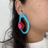 Par de aros colgantes con forma orgánica, compuestos por una estructura de acrílico celeste y una pieza superpuesta de acrílico rojo con detalle rosa.