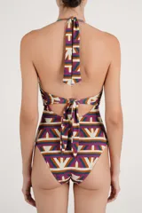 Malla enteriza con estampado geométrico multicolor en tonos beige, fucsia, verde y naranja. Presenta diseño halter con argolla central de madera y abertura frontal en la cintura.