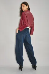 Jean de tiro medio-alto con calce holgado y relajado. Presenta piernas amplias con recortes curvos que se estrechan hacia el tobillo, creando una silueta tipo barril. Confeccionado en denim rígido color azul con sobreteñido negro, cuenta con cierre, botón y bolsillos traseros desplazados hacia el frente.