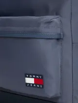 Mochila de diseño redondeado en color azul, confeccionada en poliéster. Cuenta con un compartimento principal con cierre de cremallera, un bolsillo exterior frontal con cierre, asa superior y correas acolchadas ajustables. Incluye parche distintivo de Tommy Jeans en la parte delantera.