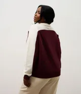 Buzo deportivo de corte oversized, con diseño bicolor en bordó y blanco. Presenta cuello alto con cierre de botones a presión, mangas largas con textura acanalada y puños elásticos.