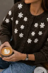 Cardigan de punto color blanco marfil, con cuello redondo, manga larga y cierre frontal de botones forrados. Presenta delicadas flores bordadas en relieve a lo largo del frente y las mangas.