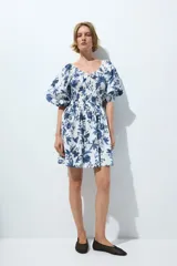 Vestido corto de algodón con estampado floral en tonos azules sobre base blanca, escote en V y mangas globo de longitud al codo. Presenta elástico fruncido en el pecho y la cintura, con falda evasé de vuelo.