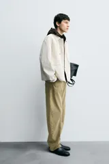 Cazadora de hombre, corte relaxed fit, color blanco hueso o crema, con acabado brillante. Presenta cuello solapa, manga larga, dos bolsillos de plastrón con solapa en la cadera y cierre frontal con botones a presión ocultos por una solapa.