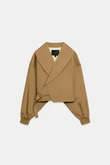 Chaqueta corta de Zara confeccionada en mezcla de algodón, con cuello solapa, manga larga con hombro caído y puños elásticos. Presenta un diseño cruzado con cierre de hebilla metálica lateral y forro interior a tono.