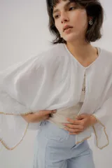 Blusa de lino color blanco, de diseño holgado, manga larga amplia acampanada con detalles de bordado en los puños y cuello redondo.