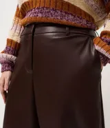 Pantalón de cuero sintético con corte barrel, de tiro alto y pierna ancha con estructura curva. Presenta bolsillos laterales tipo cuchillo y costuras decorativas con pespuntes visibles.