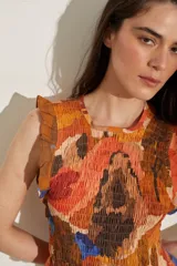 Top de lino sin mangas, con diseño fruncido en el cuerpo, cuello redondo y volados en los hombros y el ruedo. Presenta un estampado artístico en tonos celestes, verdes y rosados sobre base blanca.