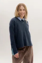 Buzo de lambswool color beige, con escote redondo y detalle en V. Presenta cierres metálicos en los puños que revelan un interior en contraste de color marrón y ribete rojo. Tiene tajos laterales para mayor comodidad y un fit amplio.