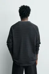 Camiseta de manga larga tipo ranglán con cuello redondo y cierre frontal de botones. Presenta un diseño de rayas horizontales finas en tonos oscuros.