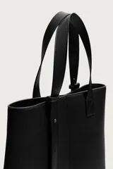 Bolso shopper de hombro en color negro, con diseño minimalista y liso. Cuenta con compartimento principal con cierre magnético y un bolsillo interior plano.