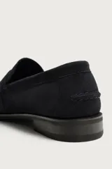 Mocasín de vestir para hombre, fabricado en piel con acabado en serraje de color azul marino. Presenta un diseño clásico con detalle de antifaz en el empeine, horma redonda, costuras visibles en el contorno y una suela sutil con ligero tacón.