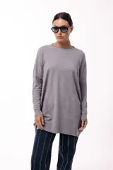 Sweater de silueta amplia y largo medio, con cuello redondo, mangas largas y detalle de botones decorativos en los laterales. Presenta un diseño de tejido de punto con caída relajada.