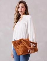 Bolso tipo tote de diseño capitoneado en color marrón, con doble asa para llevar al hombro y cierre mediante botón metálico. Cuenta con forro interno a tono y bolsillos organizadores en su interior.