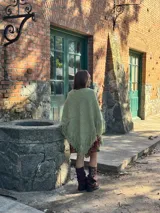 Poncho de lana merino color verde oliva, con diseño sin cuello, caída fluida y flecos en todo el ruedo.