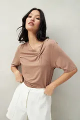 Remera blanca de manga corta con escote asimétrico y detalle de nudo con frunces en el centro del busto.