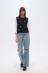 Chaleco de punto color azul marino, con cuello V y diseño de rombos trenzados. Presenta múltiples apliques bordados de motivos variados como mariposas, cerezas, flores, soles, lazos, limones, fresas, sonrisas, rosas y trozos de pizza.