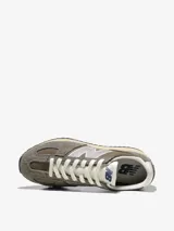 Zapatilla New Balance modelo 4717, de estilo running retro, en tonos marrón y gris topo. Presenta capellada de gamuza y malla, con el logo 'N' en plateado texturizado. Cuenta con puntera 'fang' y entresuela de EVA en color crema, y suela de goma negra con patrón de espiga.