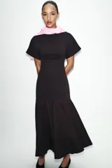 Vestido midi de color negro, confeccionado en tejido de punto con cuello barco y manga corta. Presenta un diseño ajustado en el torso que se combina con una falda inferior con vuelo y acabado evasé.