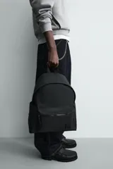 Mochila negra lisa con acabado engomado, compartimento principal con cierre de cremallera, bolsillo interior con cremallera, bolsillo frontal con cremallera, parte posterior acolchada con banda de sujeción para equipaje, asa de mano y dos asas de hombro ajustables y acolchadas.