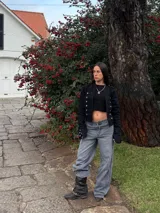 Campera estilo militar de color negro, con cuello mao y cierre frontal. Presenta múltiples botones metálicos plateados dispuestos en filas horizontales y detalles de charreteras en los hombros. Las mangas cuentan con puños decorados con botones a juego.