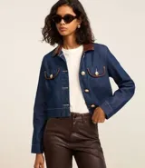 Campera de jean azul con cuello inglés de poliuretano color marrón. Cierre frontal con botones metálicos. Bolsillos de parche en el pecho con detalle de ribete de poliuretano marrón.