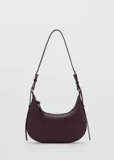 Bolso de hombro tipo hobo en color bordó, con diseño de media luna, cierre de cremallera superior y asa ajustable con hebillas metálicas.