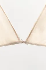 Sujetador triangular de escote en pico con detalle de lazo central y acabados en ondas. Presenta un tejido con textura pointelle y tirantes ajustables.