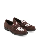 Zapato tipo mocasín de gamuza color marrón, con detalle de pelo sintético con estampado de vaca en la parte superior y suela plana de goma.