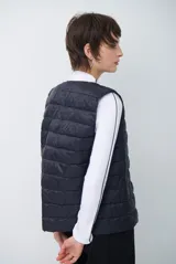 Chaleco acolchado tipo puffer, color beige, sin mangas, con cuello redondo y cierre frontal con botones a presión.