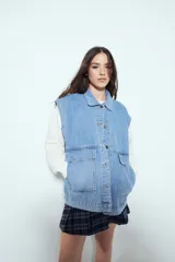 Chaleco de jean con corte oversized, diseño sin mangas, cuello camisero, cierre frontal con botones metálicos y bolsillos frontales tipo cargo.