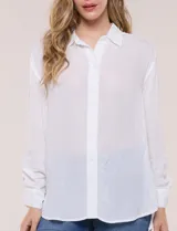 Camisa Magaschoni de silueta holgada y tejido texturizado color blanco, con cuello camisero, cierre frontal de botones, mangas largas con presilla para arremangar y diseño asimétrico con espalda más larga.