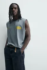 Musculosa de corte relajado con efecto lavado, cuello redondo y sisas amplias. Presenta estampados gráficos en color amarillo en el frente y acabados irregulares que le otorgan una apariencia única.