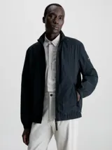 Campera negra de nailon arrugado reciclado, con cuello alto, puños y bajo elásticos, cierre con cremallera, bolsillos con cremallera en la cintura, abertura de ventilación en la espalda, forro de poliéster reciclado e insignia con el logo de goma de Calvin Klein en la manga.