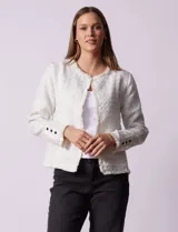 Chaqueta de tejido tweed color blanco con destellos brillantes, de corte recto y estructurado. Presenta cuello a la base, abertura frontal y puños decorados con botones en contraste. Los bordes del cuello, la cartera frontal y el ruedo cuentan con una terminación deshilachada.
