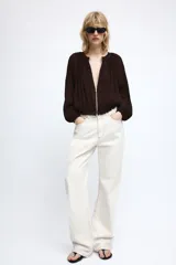 Chaqueta de organza plisada color marrón oscuro, con cuello redondo, cierre frontal con cremallera metálica, mangas largas con puños elásticos y bajo con acabado elástico.