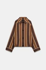 Chaqueta tipo bomber de cuello solapa y manga larga, con cierre frontal de botones y bolsillos de vivo en el delantero. Presenta un diseño a rayas verticales en tonos marrones y beige.
