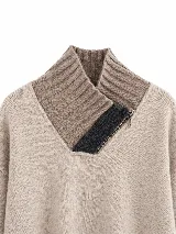 Polera tejida en lambswool color gris, con cuello alto y cierre frontal parcial con detalle en negro. Presenta diseño de tajos laterales en el ruedo, puños acanalados con detalle de rayas en contraste y un pequeño aplique circular con logo en el frente.