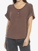 Remera de manga corta color marrón con cuello amplio tipo scoop y tapeta frontal con botones. Presenta un calce relajado y costuras visibles que acentúan su estilo casual.
