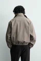 Cazadora cropped de hombre con tejido de estructura espiga. Presenta cuello subido con cierre de botones, cierre frontal de cremallera, bolsillos laterales con solapa y acabados elásticos en puños y cintura.